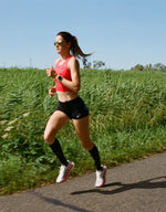 Woman running in full motion with green plants behind her.