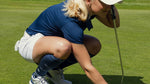 Romy Meekers kneeling on a golf course with a cap on.