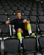 Man sitting in between black chairs wearing bright yellow compression socks.