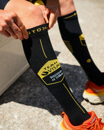 A person wearing a high black sock with yellow details.
