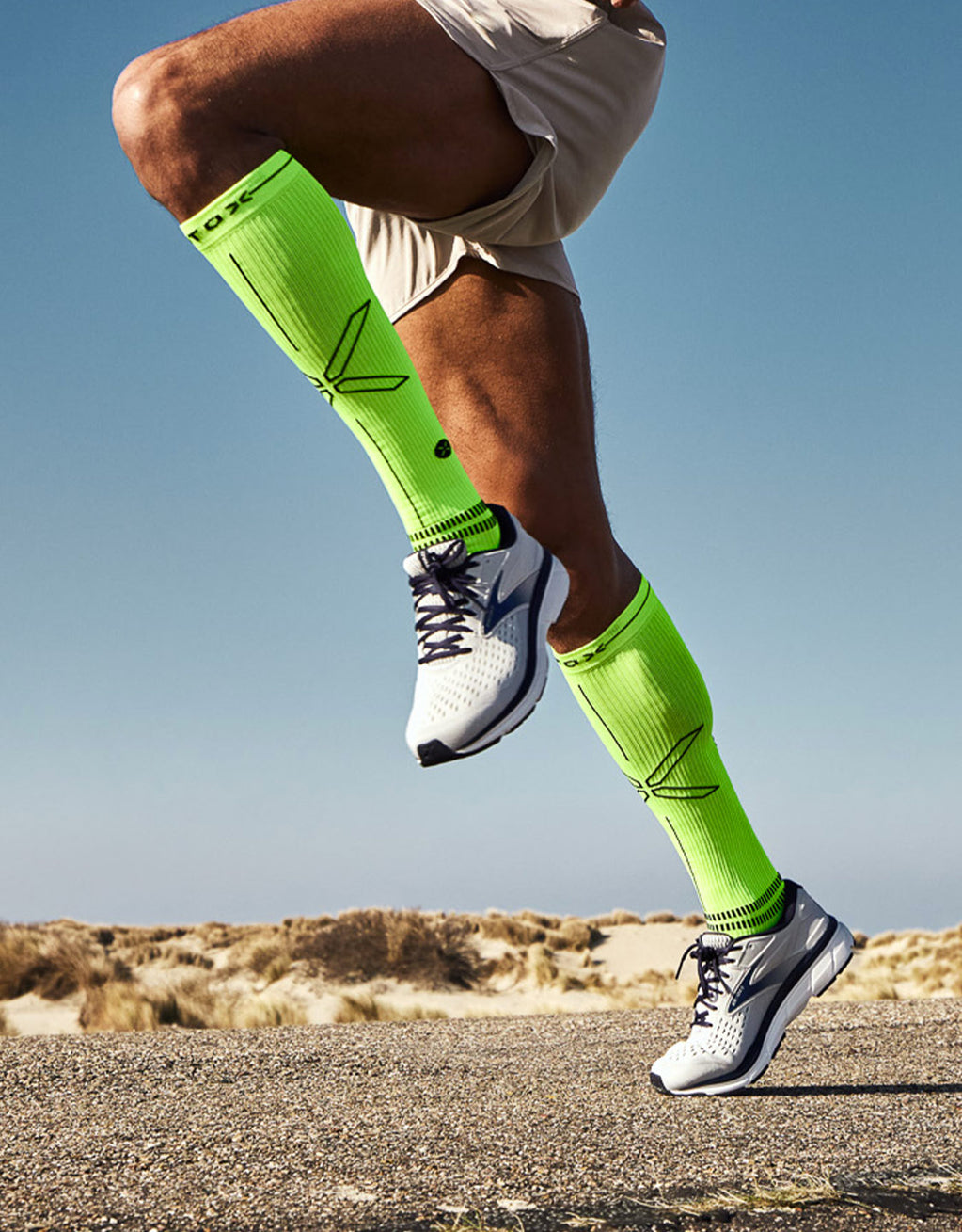 Yellow socks with a X on them running towards the sun with sand in the background.