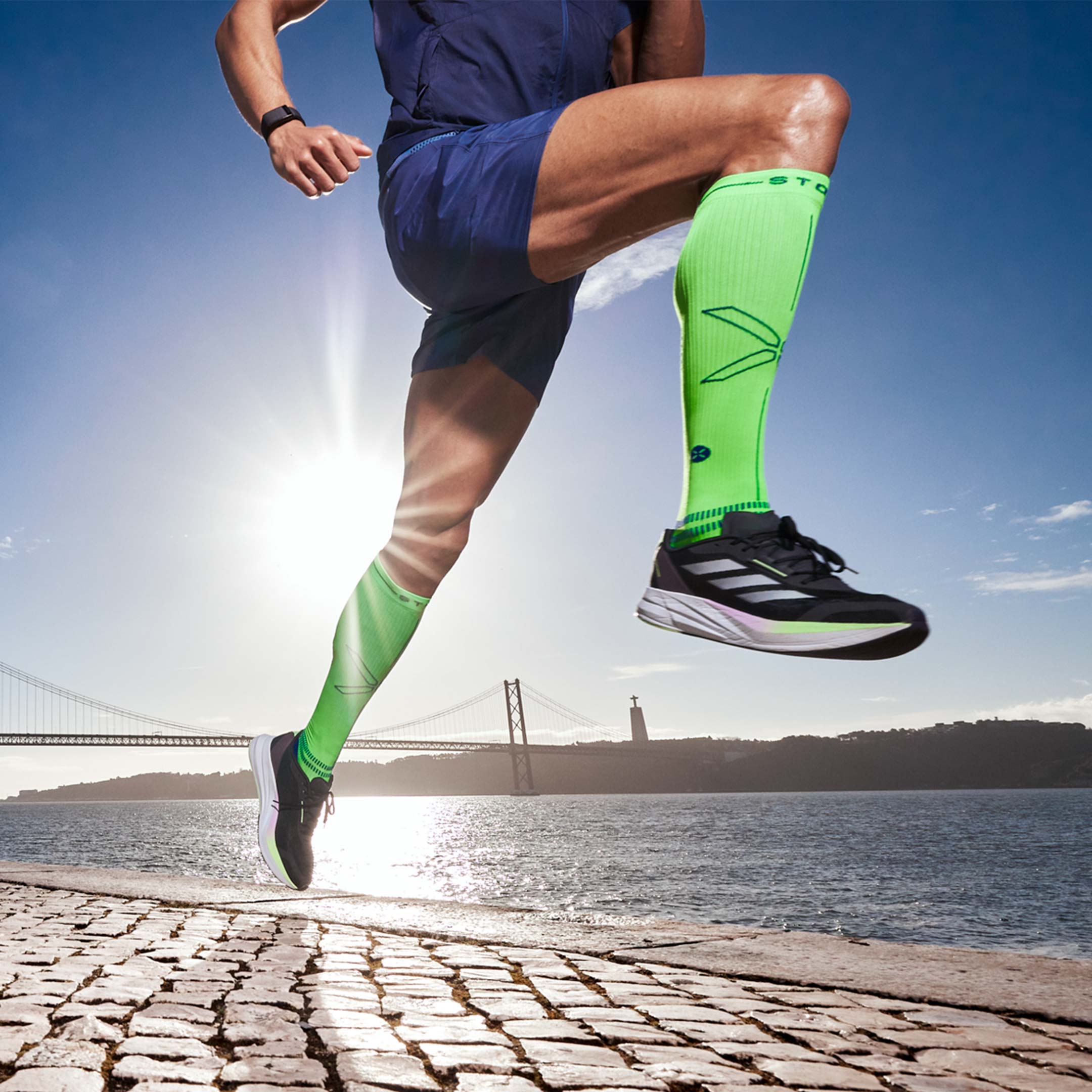 Man running next to water with neon sock on. 