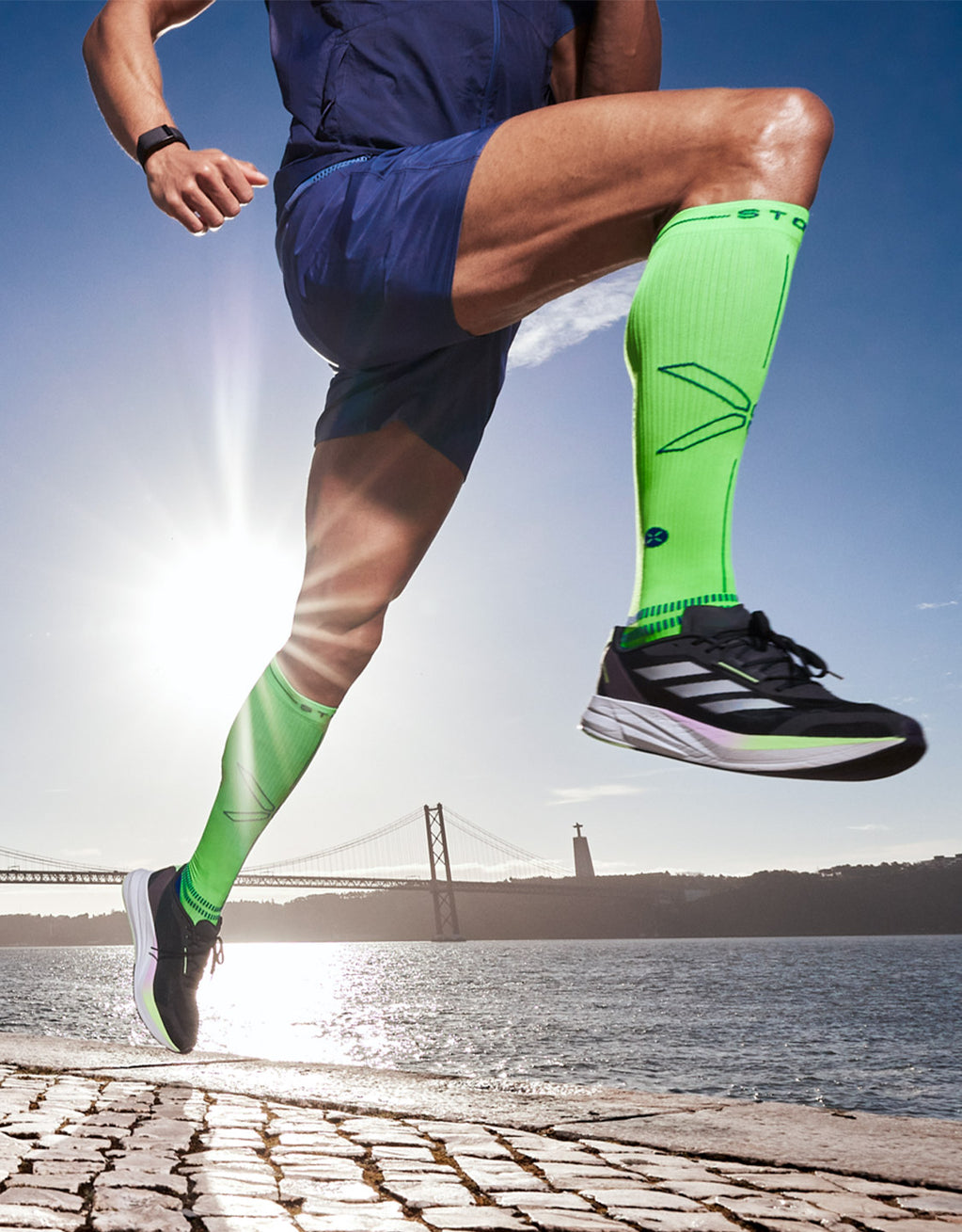 Man running next to water with neon sock on.