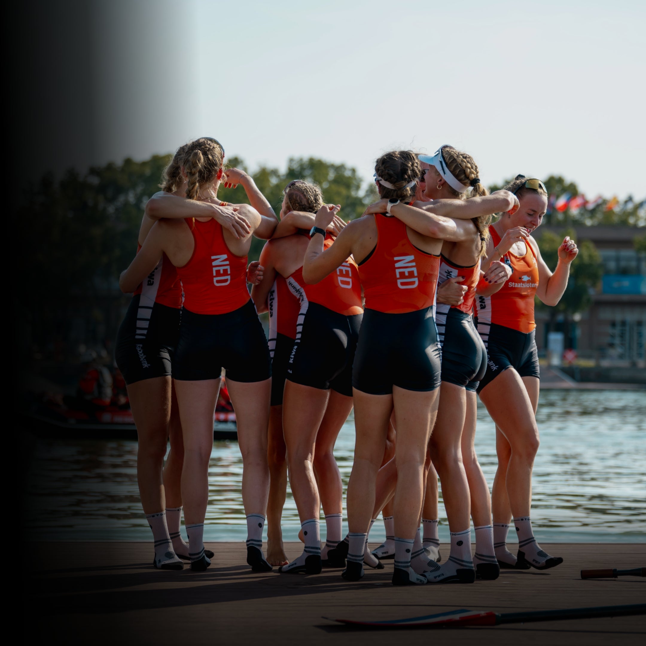 Rowing team huddled together on a dock by a body of water