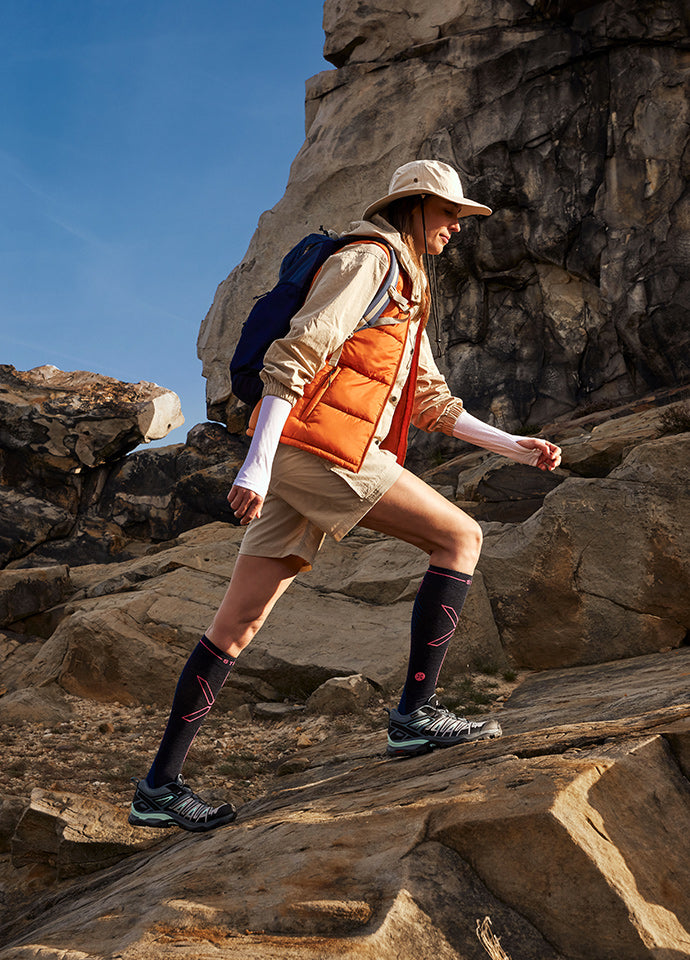 Woman walking over rocks wearing hiking compression socks in the sun.