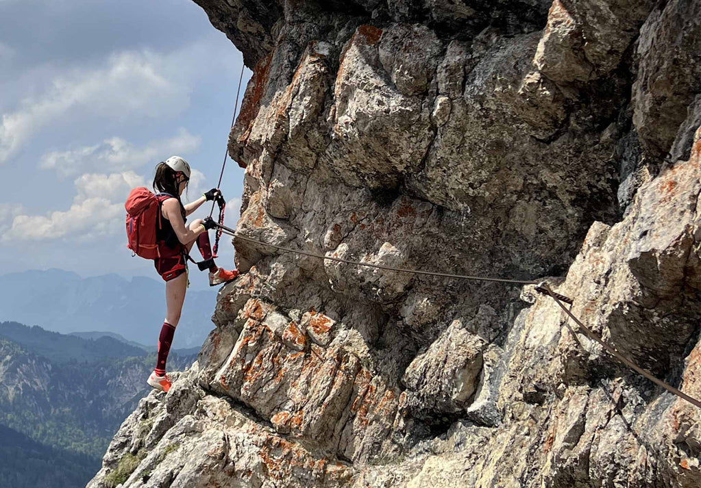 Woman climbing large rocky mountain whilst securing her safety line.