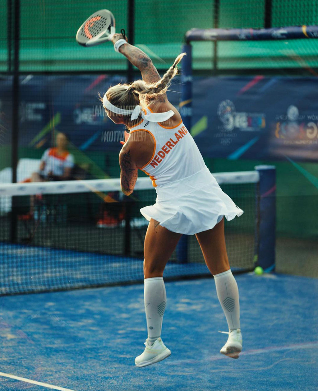 Woman playing padel in alle white outfit on a blue court.