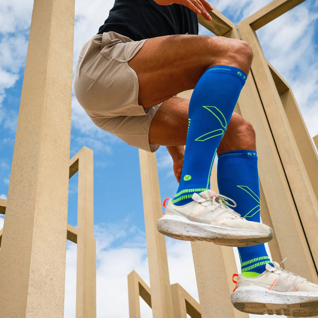 Man jumping wearing beige shorts and blue knee high compression socks. 