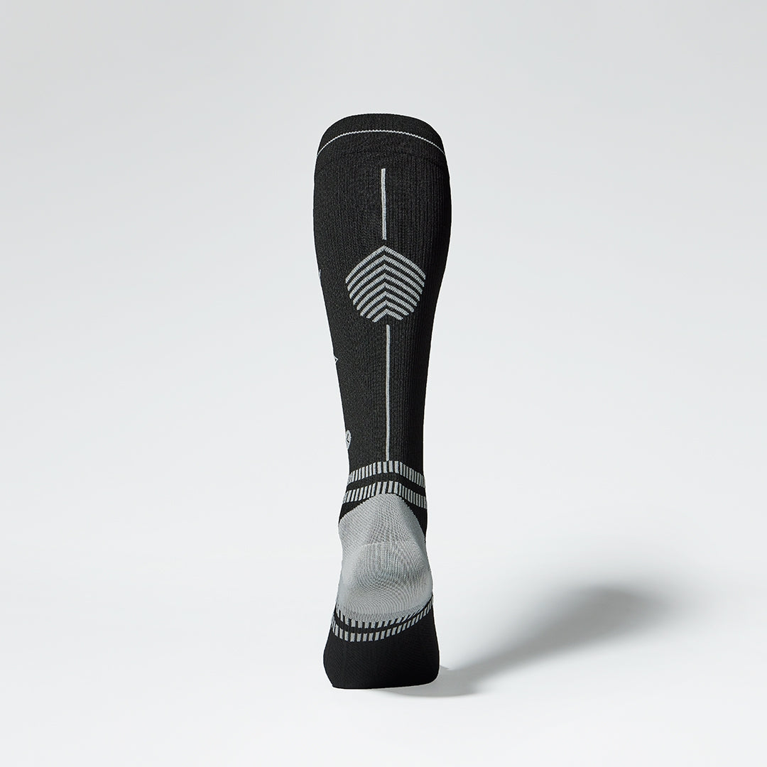 View of the back of a knee high compression sock in black with grey details. 