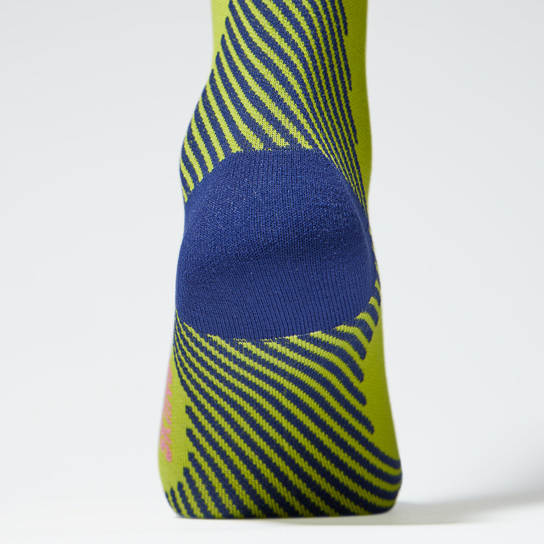 Close up of a yellow compression sock with a blue heel and lined details.