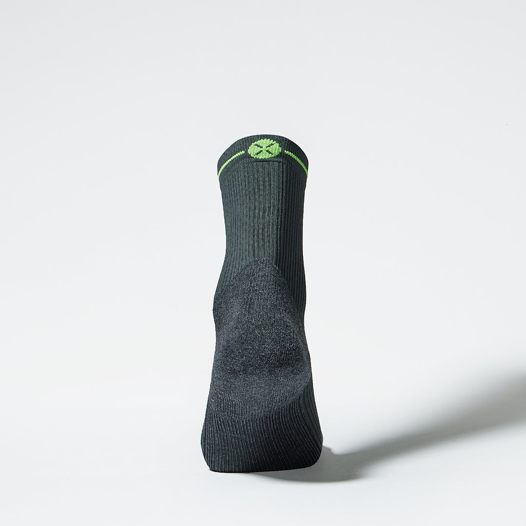 View of the back of an ankle high compression sock in dark grey with green accents. 