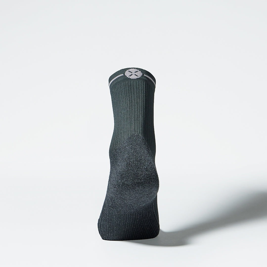 View of the back of an ankle high compression sock in dark grey. 