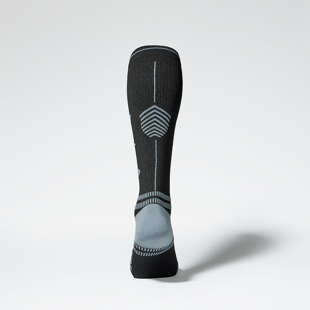  Back view of a knee high compression sock in black with grey heel. 