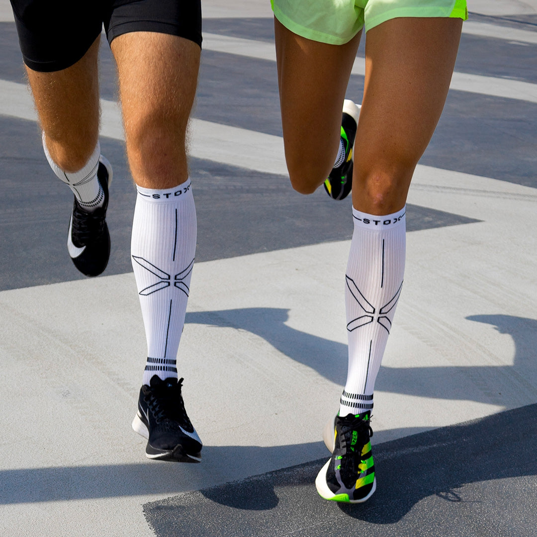 The legs of two people running with white sports compression socks. 