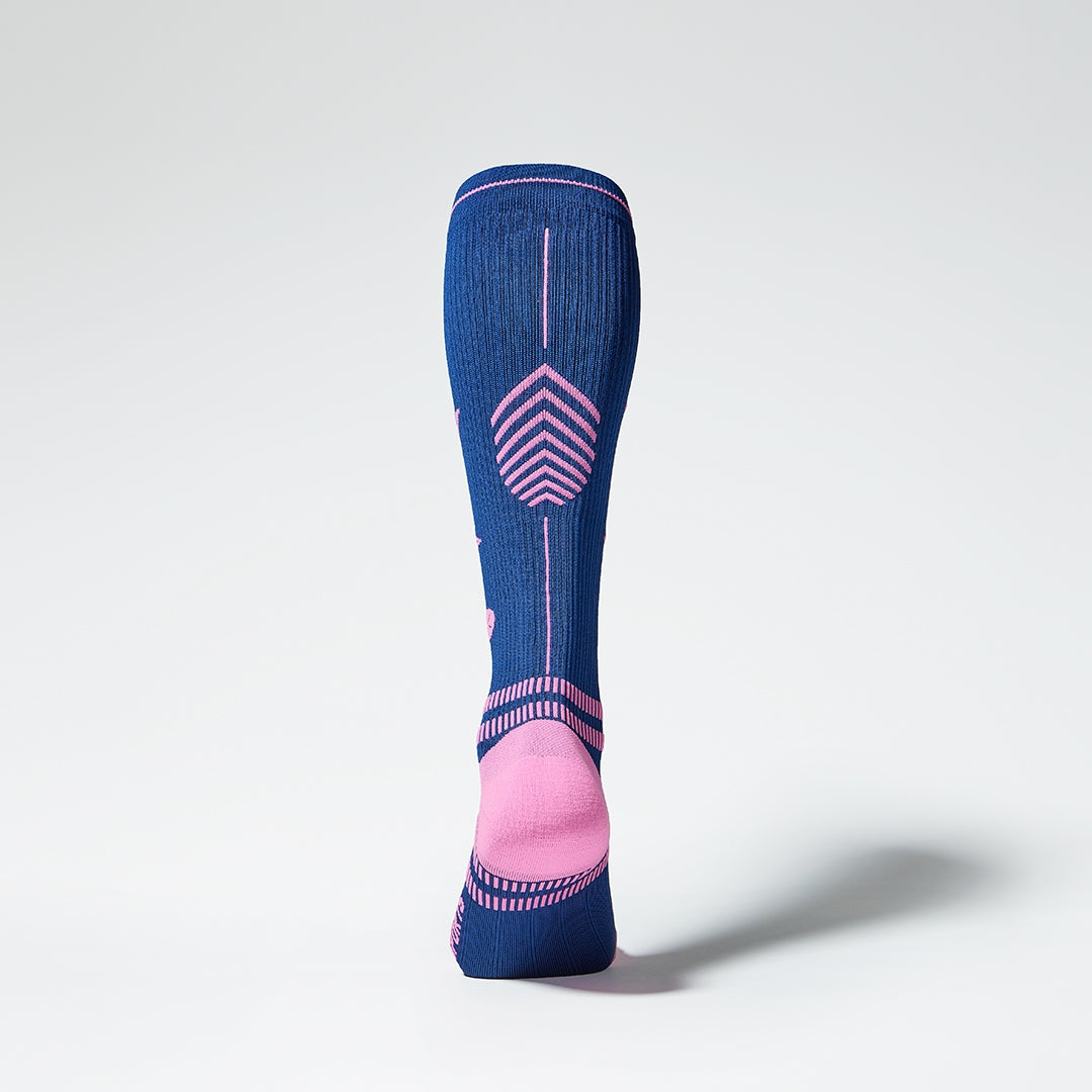 View of the back of a knee high compression sock in dark blue with pink accents. 
