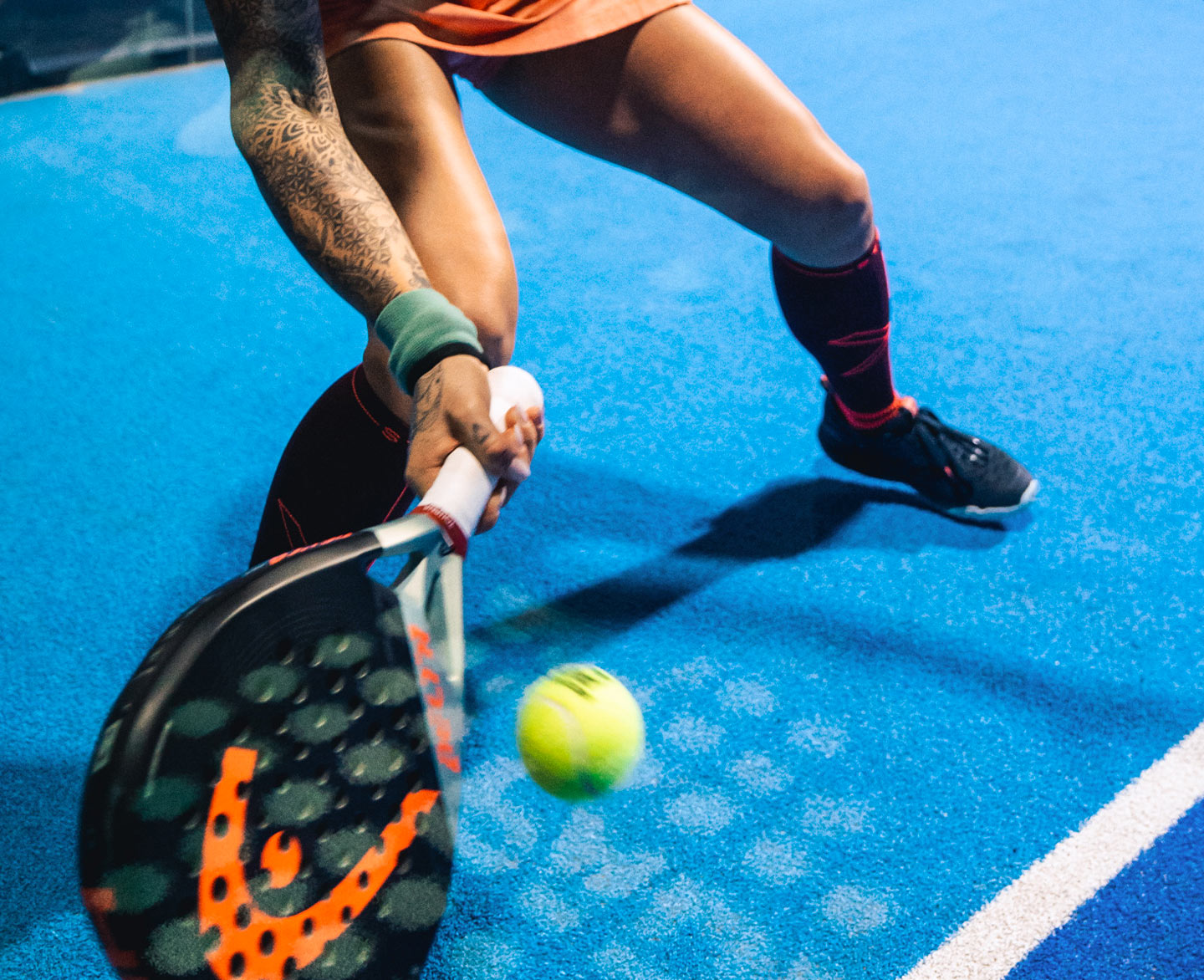 Woman hitting a ball with her black and orange padel racket.