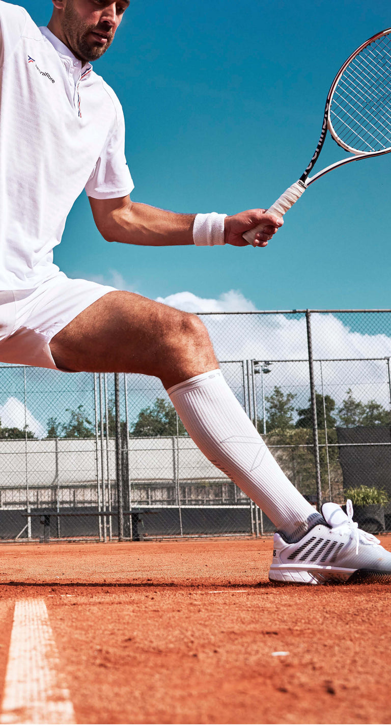 Tennis player in all white outfit playing on gravel. 