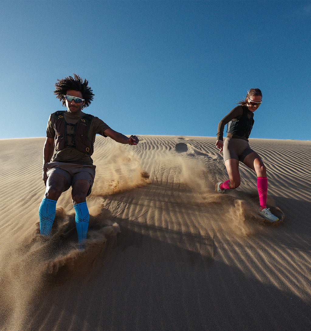 Two people running on sand dunes with a clear blue sky.