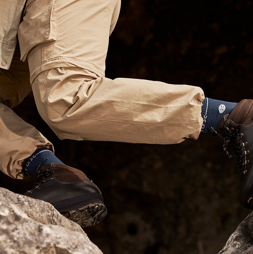Person wearing beige pants and dark boots and STOX socks on a rocky surface