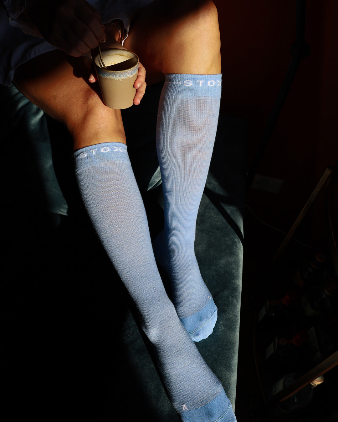 Woman sitting on couch with compression socks and coffee.