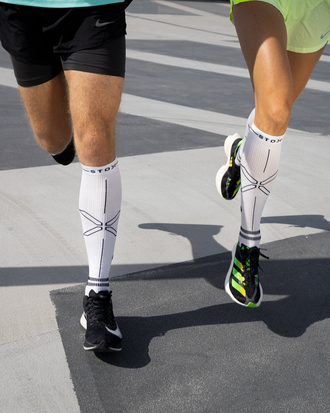 Couple running on a grey floor with compression socks.