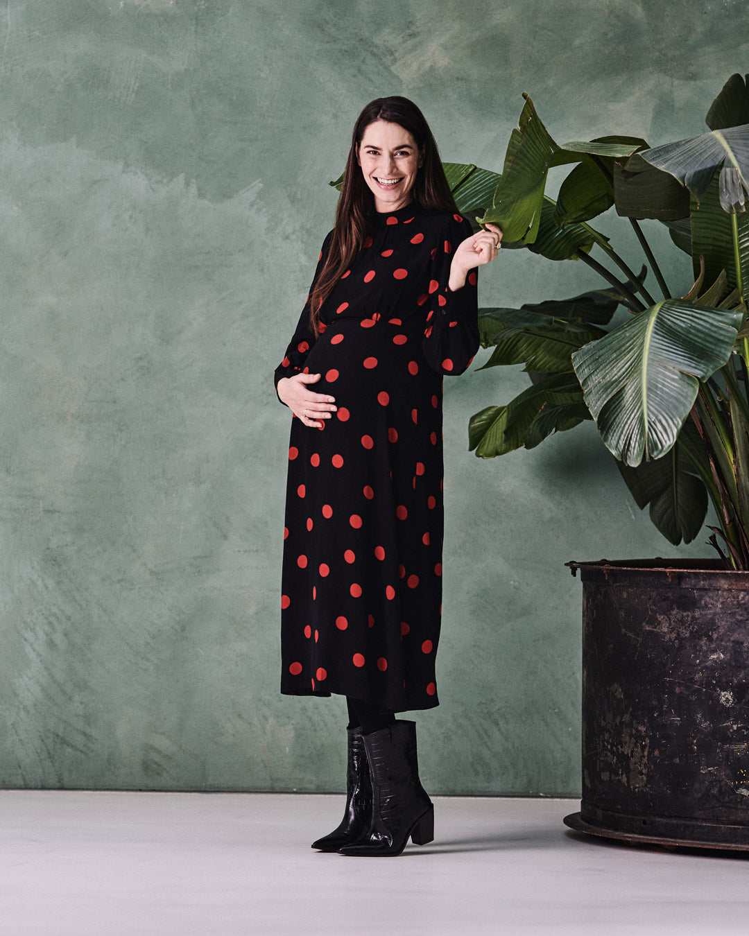 Pregnant woman standing next to a plant with compression socks.