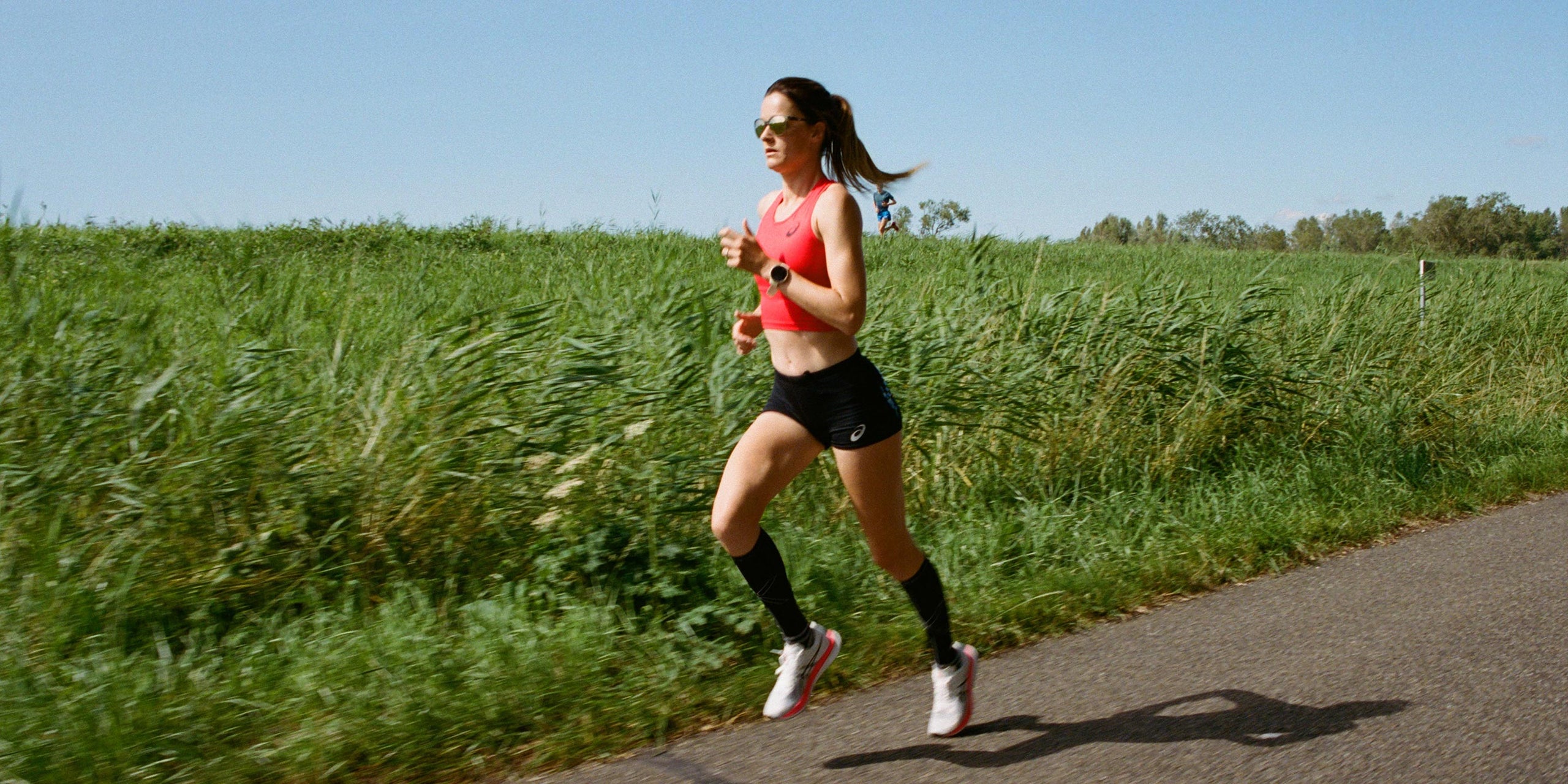 Woman running in full motion with green plants behind her. 