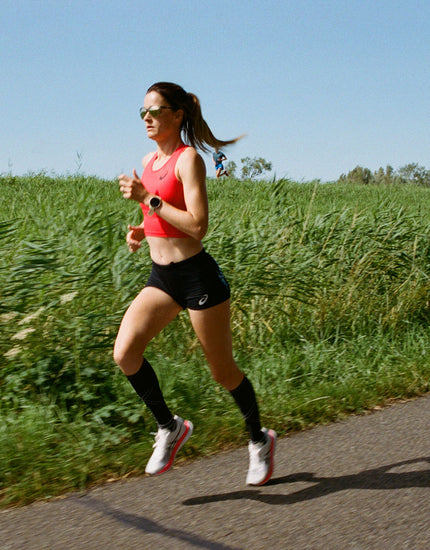 Woman running in full motion with green plants behind her. 