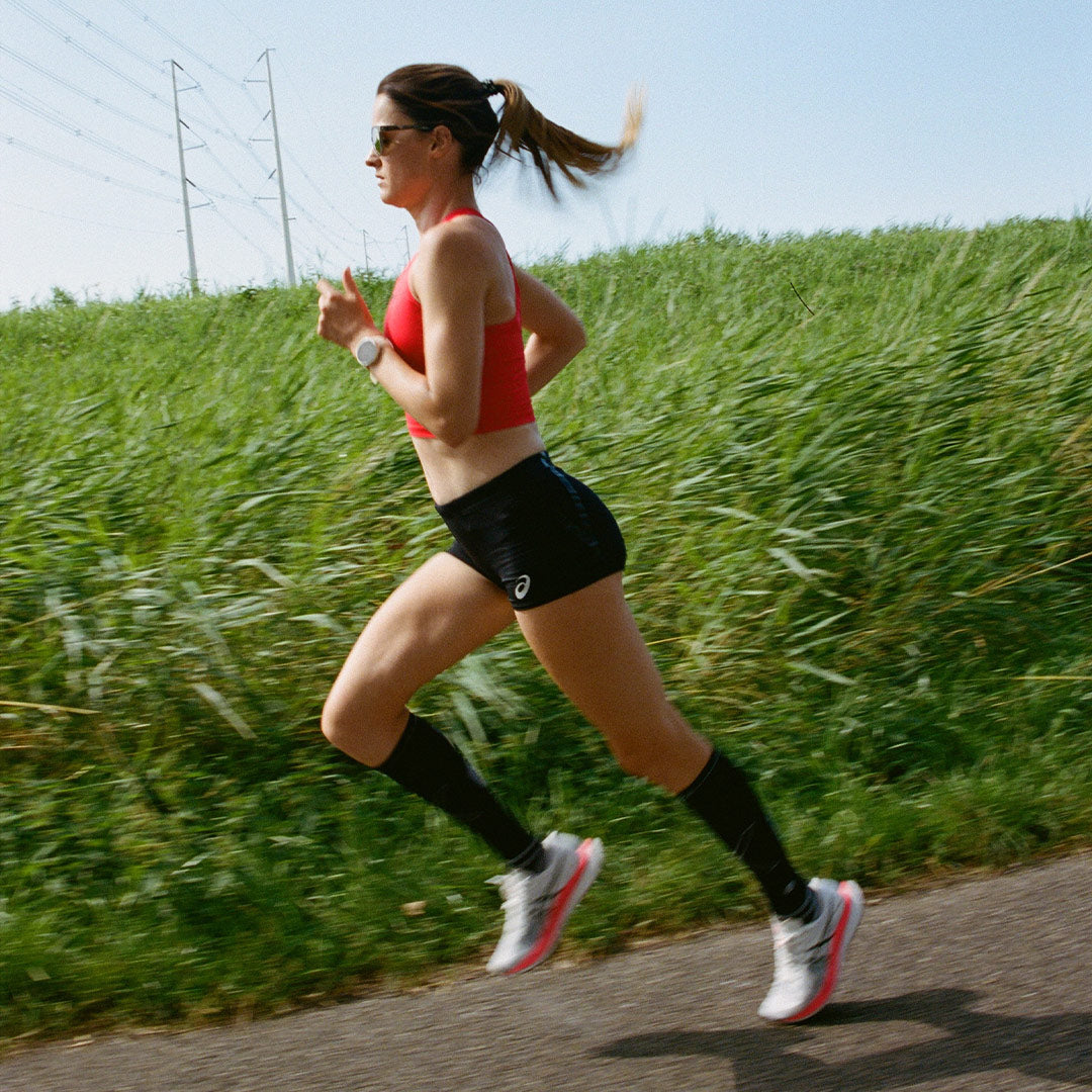 Woman running in full motion with green plants behind her. 