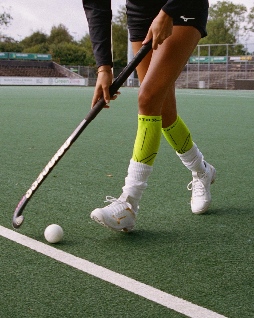 Woman running across a field hockey field with white shoes. 