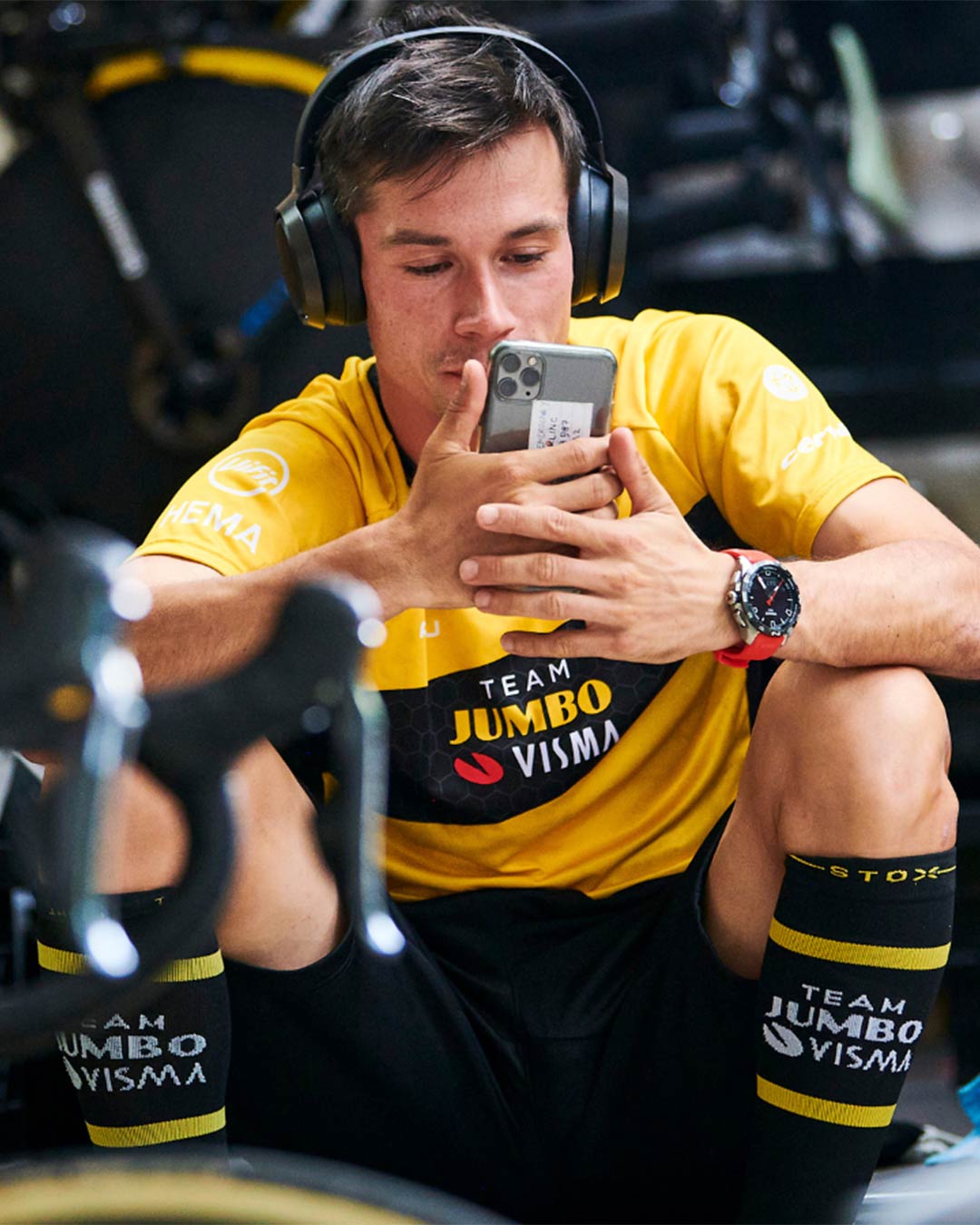 Primoz Roglic wearing headphones and looking at his telephone.
