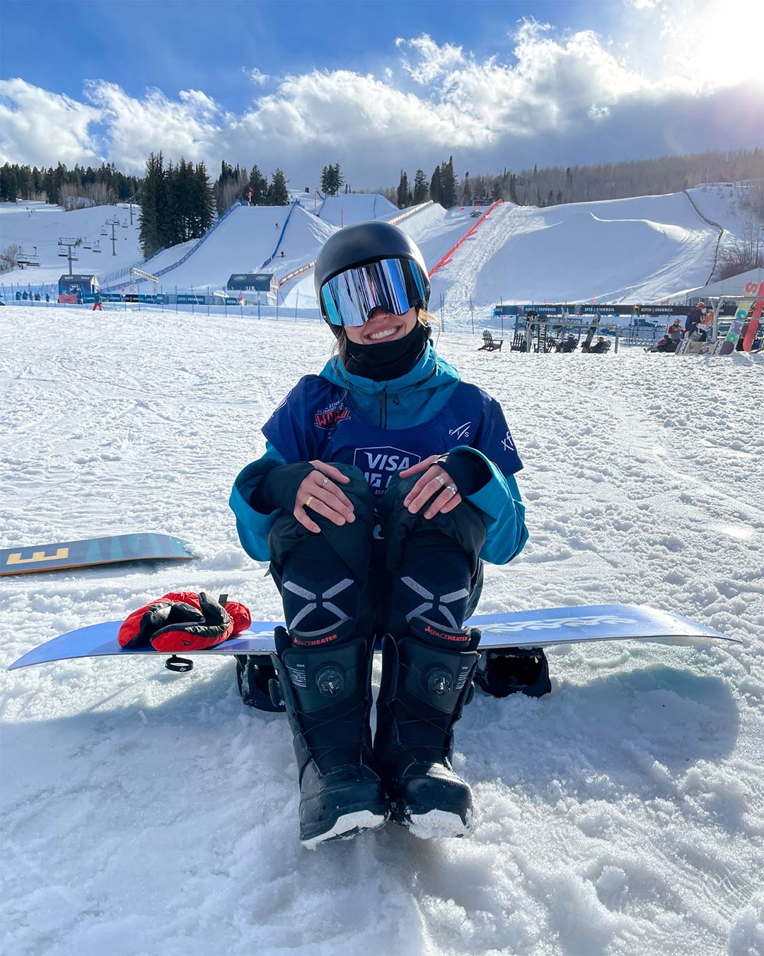 Loranne Smans sitting on a blue snowboard in front of the slopes.