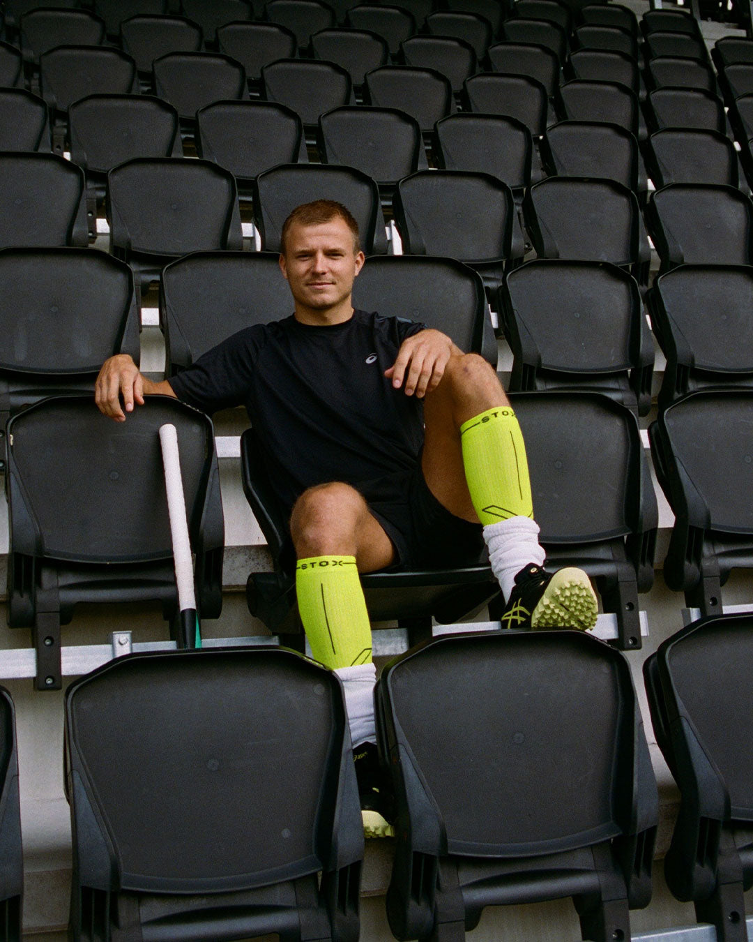 Man sitting in between black chairs wearing bright yellow compression socks. 