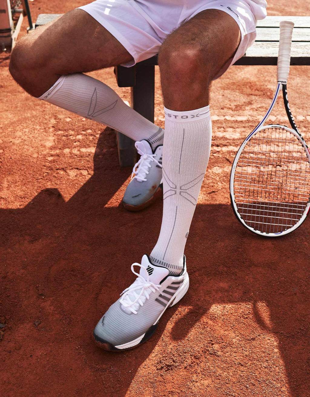 A seated person wearing white socks with a tennisracket. 