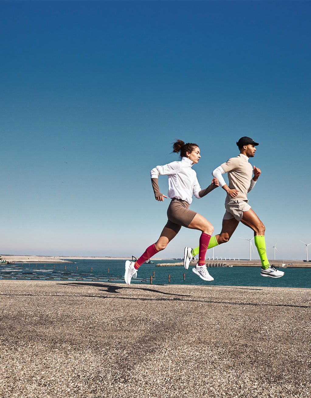 Two people running on a dam with water in the background.