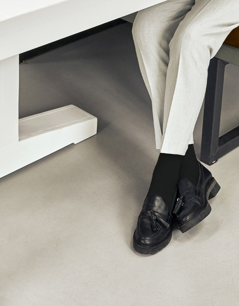 Two legs underneath a table with black shoes and socks. 