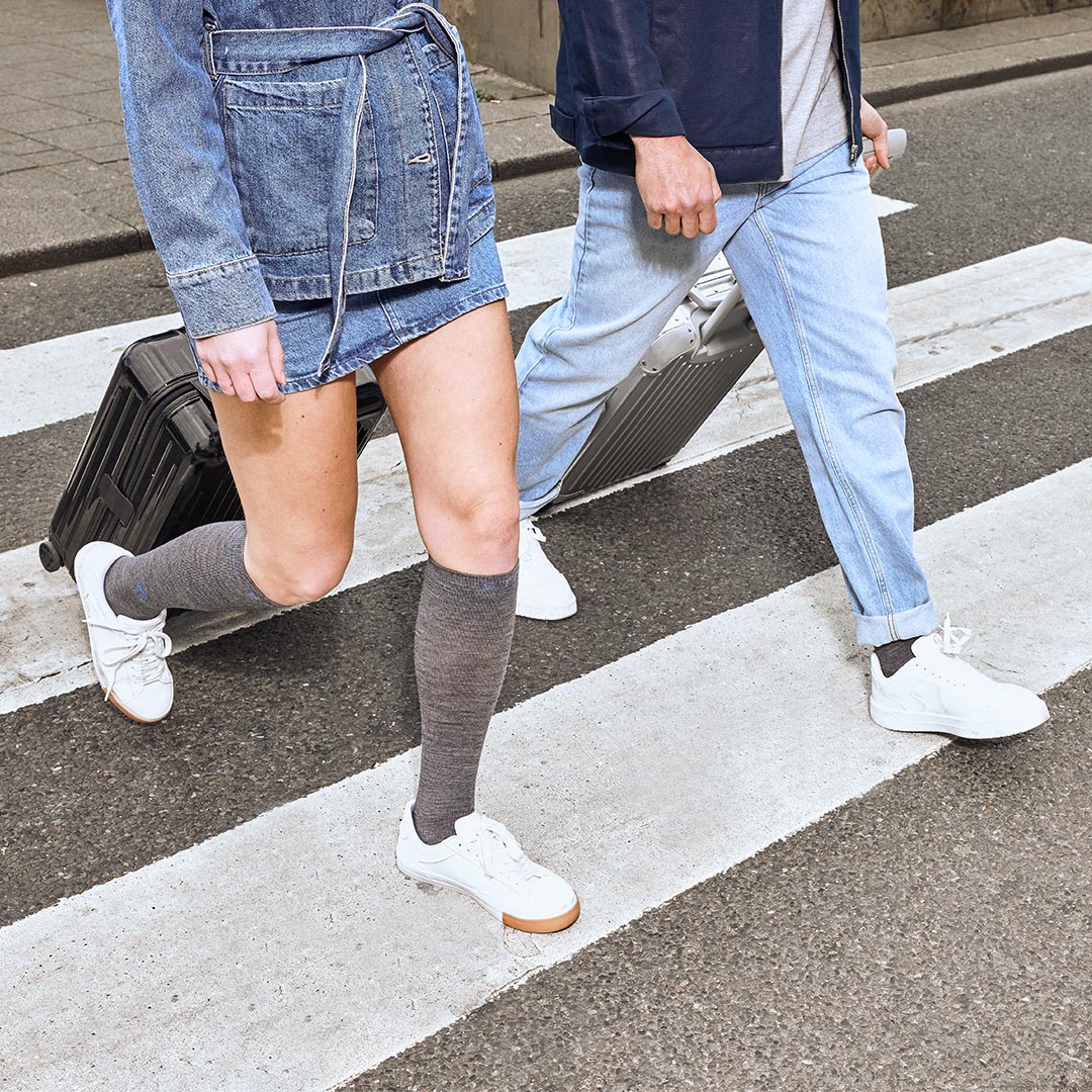 People wearing jeans and grey socks walking across a crossroad. 