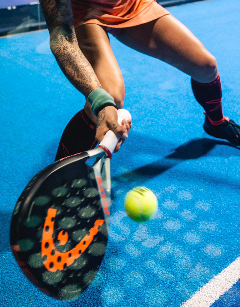 Woman playing and her padel racket is hitting a ball.