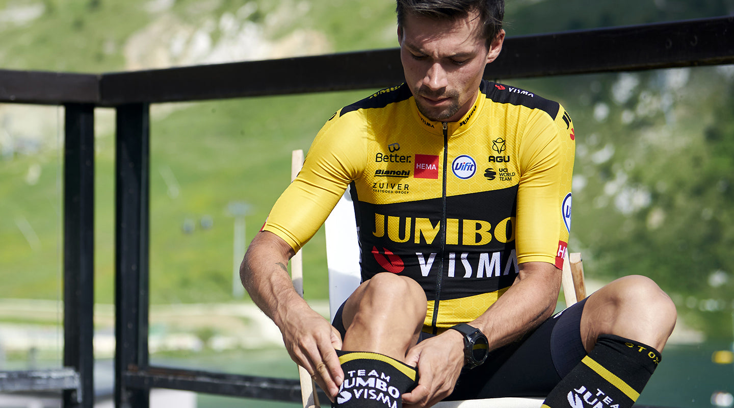 Primoz Roglic sitting down and pulling up his recovery compression socks. 