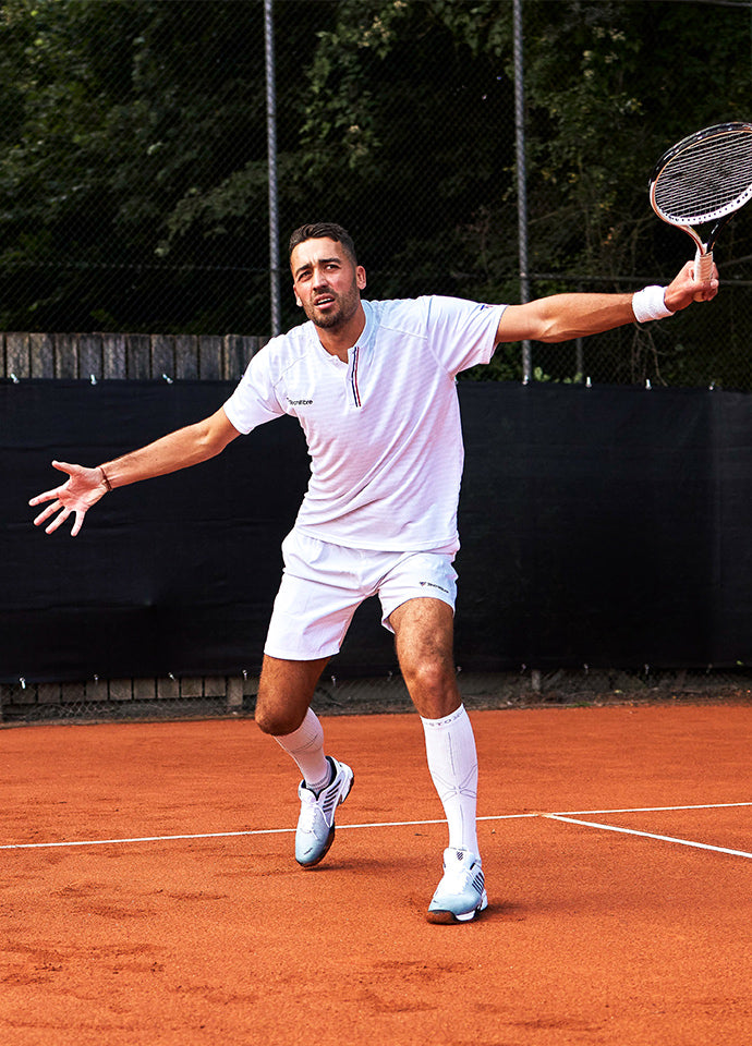 Man playing tennis while standing in a wide stance.