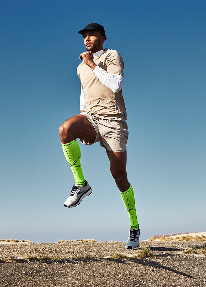Man running whilst wearing bright yellow compression socks and beige clothing. 