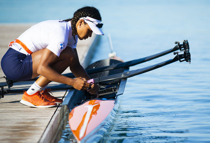 Woman kneeling over orange rowing boat in the sun. 