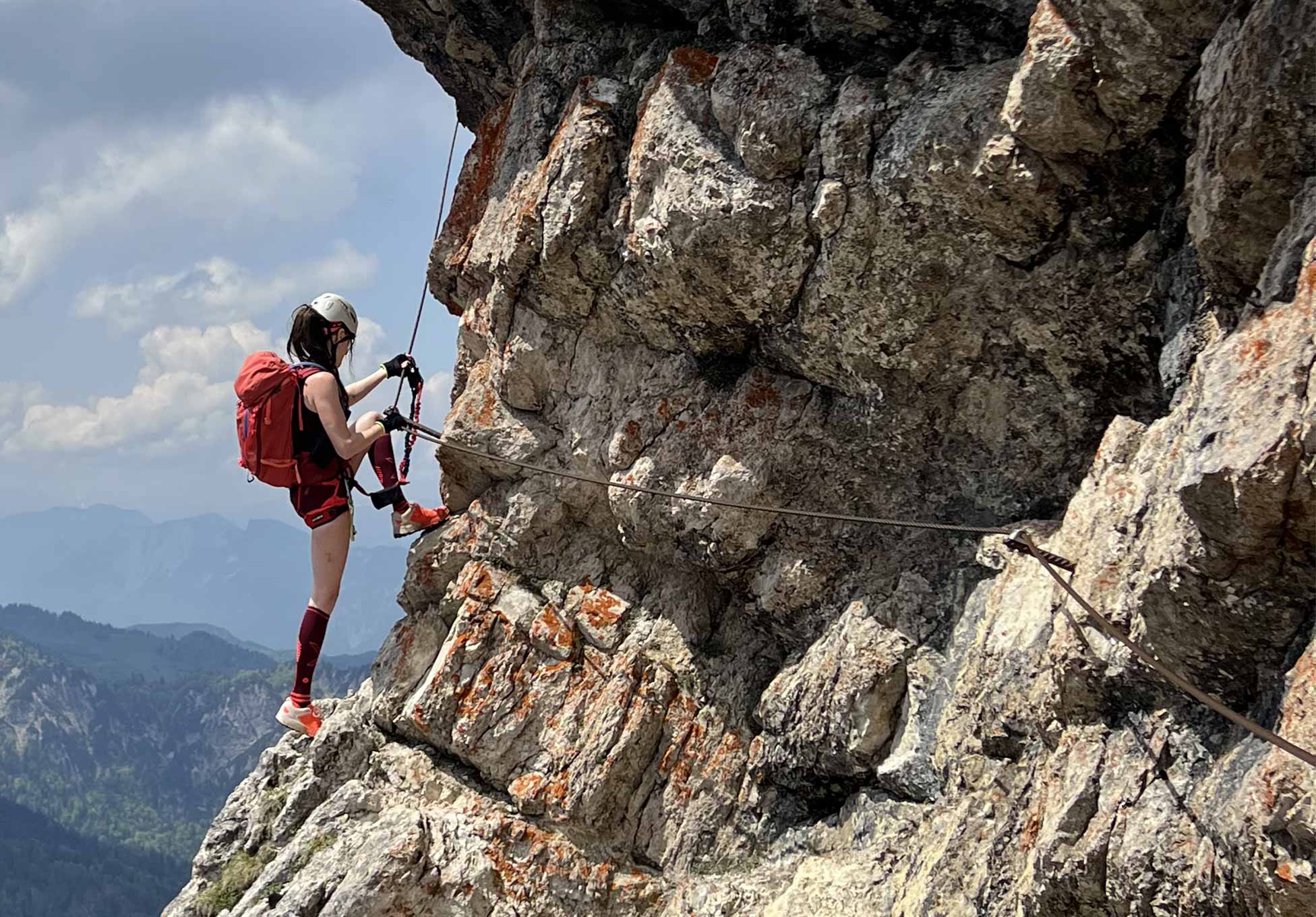 Woman climbing large rocky mountain whilst securing her safety line. 