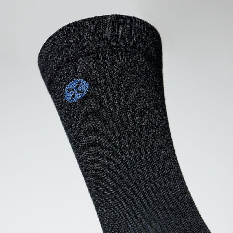 A close up of a black mid calf compression sock with a blue logo.