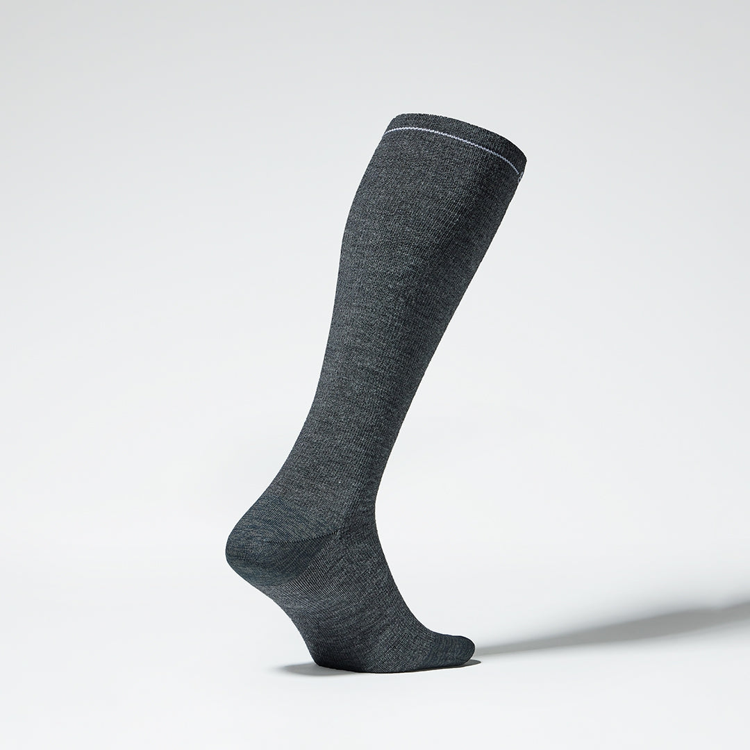 Dark grey knee high compression sock with white details seen from the side. 