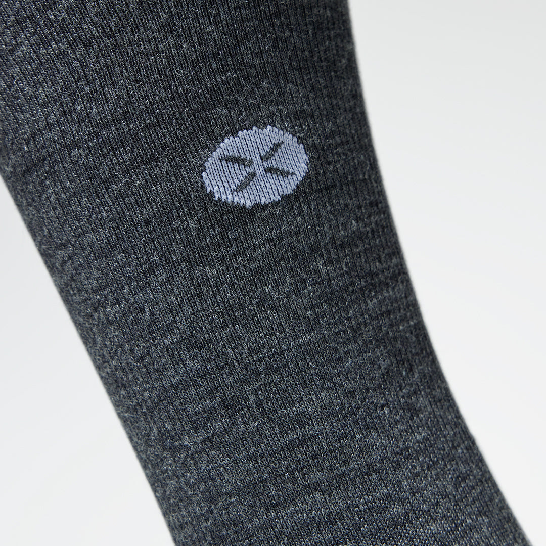 A close up of a dark grey compression sock with a little white logo.