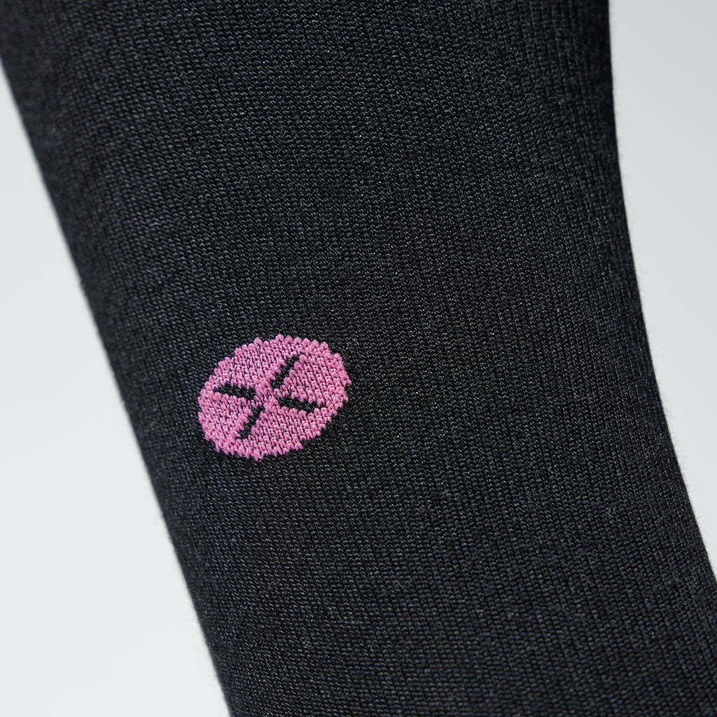 A close up of a black compression sock with a little fuchsia logo. 
