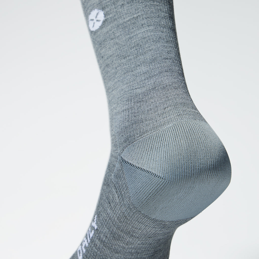 A close up of a silver grey high compression sock with a little white logo.
