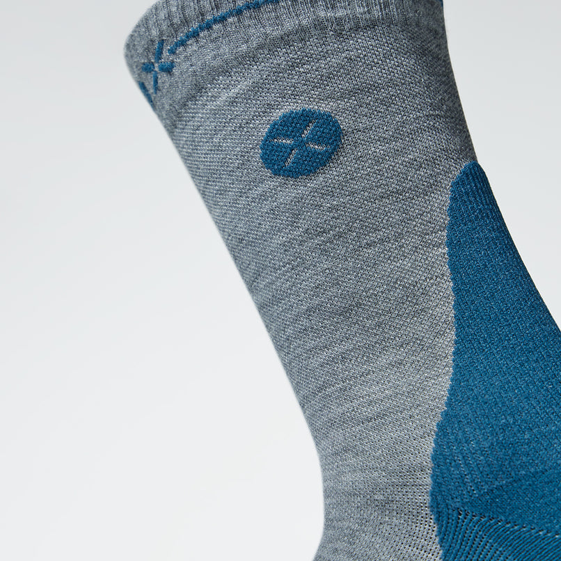 Close up of a ankle high compression sock in silver grey with a teal logo.