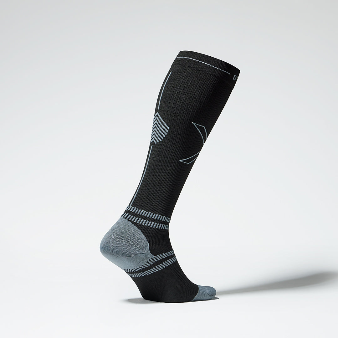 Side view of a standing black sock with grey heel. 